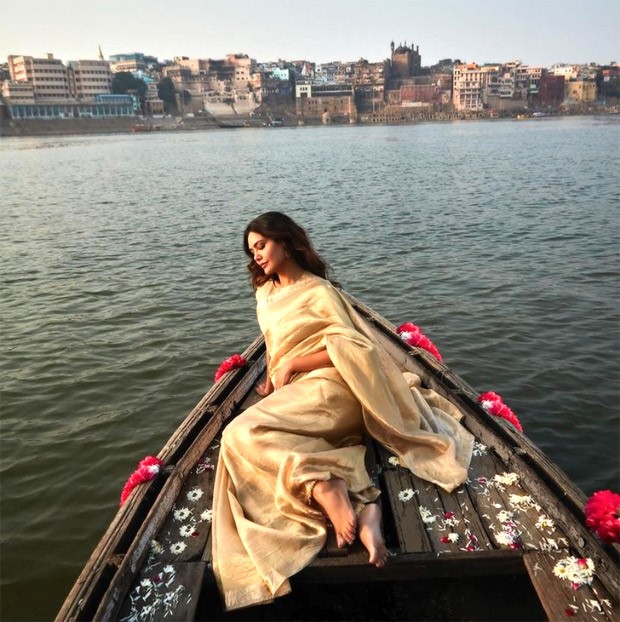 Esha Gupta radiates ethereal elegance in a golden saree against the backdrop of Benaras ghats